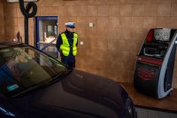 zdjęcie kolorowe - samochód na hali diagnostycznej - policjant patrzy na monitor z wynikiem badania hamulców