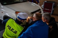 zdjęcie kolorowe - samochód - policjant, diagnosta i kierowca kucają przy przedniej lampie - wskazują nieprawidłowości