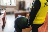 zdjęcie - pomieszczenie na krześle siedzi zatrzymany a za nim stoi policjant