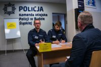 wnętrze komendy dwóch policjantów przy biurku i rezerwista