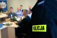 ramie policjanta w mundurze z napisem &quot;Policja&quot; w tle siedzący uczestnicy ćwiczeń