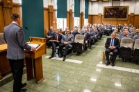 zdjęcie kolorowe przedstawia uroczystość pożegnania odchodzącego komendanta - sala sesyjna w tle siedzący goście a na pierwszym planie przy mównicy zastępca komendanta