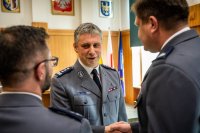 zdjęcie kolorowe przedstawia uroczystość pożegnania odchodzącego komendanta - sala sesyjna komendant i dwóch policjantów składających życzenia