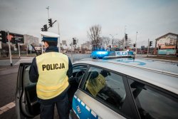 na pierwszym planie radiowóz i policjant stojący obok, w tle skrzyżowanie