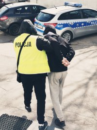 zdjęcie - policjant z zatrzymanym w drodze do radiowozu