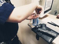 zdjęcie - policjant dezynfekuje ręce w tle okienko i broń