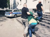 policjant prowadzi zatrzymanego do budynku komendy