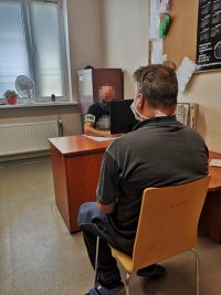 zdjęcie przedstawia zatrzymanego siedzącego tyłem, przed nim policjant przy biurku
