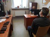 zdjęcie przedstawia policjanta przesłuchującego zatrzymanego siedzącego tyłem, po lewej stronie na biurku widoczne telefony zarekwirowane zatrzymanemu