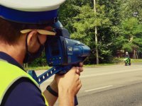 zdjęcie przedstawia policjantów w trakcie działań - policjant dokonujący pomiaru prędkości motocyklisty