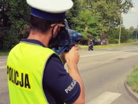 zdjęcie przedstawia policjantów w trakcie działań -  policjant dokonujący pomiaru prędkości motocyklisty