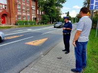 zdjęcie z kontroli oznakowania dróg w rejonie szkół - policjant i urzędnik zwracają uwagę na oznakowanie namalowane na jezdni