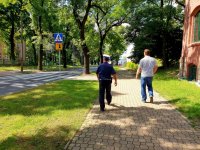 zdjęcie z kontroli oznakowania dróg w rejonie szkół - policjant i urzędnik idą chodnikiem w stronę przejścia dla pieszych przy szkole