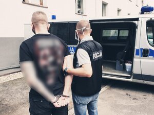 zdjęcie przestawia policjanta kryminalnego z zatrzymanym przy policyjnym radiowozie