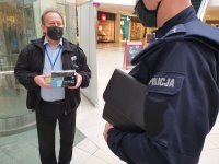 na zdjęciu policjant i pracownik ochrony z pudełkiem maseczek w ręku