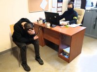 zdjęcie kolorowe - pomieszczenie biurowe, zatrzymany siedzi na krześle policjant za biurkiem