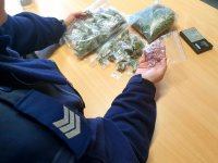 zdjęcie kolorowe - pomieszczenie biurowe, policjant pokazuje narkotyki leżące na stoliku