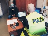 policjant przesłuchuje zatrzymanego siedzącego na krześle w pomieszczeniu biurowym