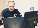 zdjęcie przedstawia policyjnego profilaktyka przy laptopie w trakcie zajęć online