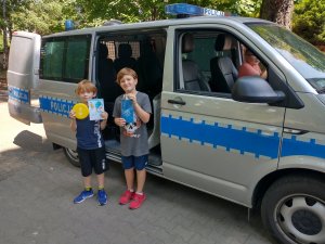 Wizerunek dzieci na tle radiowozu z otrzymanymi gadżetami.