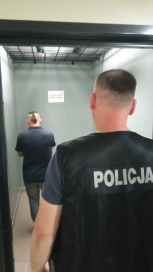 Widok sprawcy rozboju w Sądzie pilnowanego przez policjanta.
