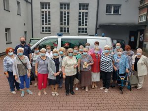 Grupa seniorów pozująca do zdjęcia na tle radiowozu