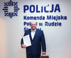 Marian Świerc z pamiątkową teczką na tle napisu Policja