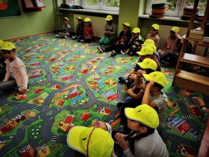 dzieci siedzą na dywanie w odblaskowych czapkach na głowach