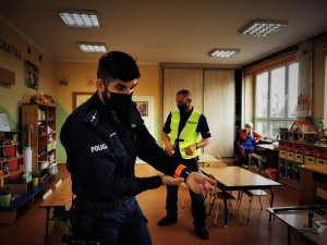 policjant pokazuje jak nosić odblaskową opaskę