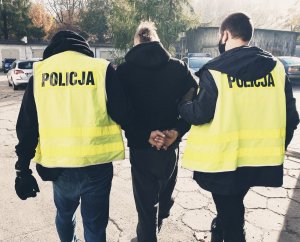 policjanci prowadzą zatrzymanego przez parking komendy