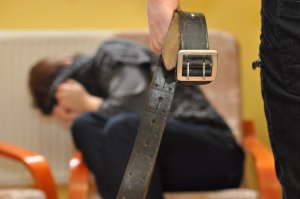 zdjęcie poglądowe kobieta zasłania głowę, na pierwszym planie ręka mężczyzny trzymająca pas od spodni