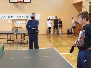 sala gimnastyczna, stół do tenisa, policjant przygląda się grze uczestników