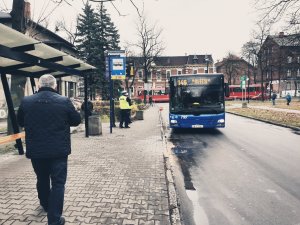 policjanci kontrolują obowiązek zakrywania ust i nosa w autobusach - na zdjęciu autobus wjeżdżający na przystanek, w tle policjanci, na pierwszym planie idący mężczyzna