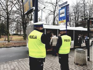 policjanci kontrolują obowiązek zakrywania ust i nosa w autobusach - na zdjęciu policjanci na przystanku, w tle autobus
