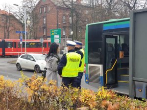 policjanci kontrolują obowiązek zakrywania ust i nosa w autobusach - na zdjęciu autobus i policjanci z kobietą na chodniku obok