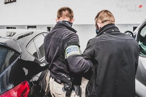 zdjęcie poglądowe, parking, zaparkowane samochody, policjant i zatrzymany mężczyzna
