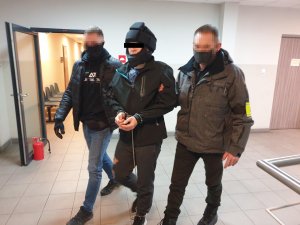 dwóch policjantów kryminalnych prowadzi zatrzymanego korytarzem