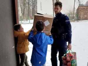 policjant i dzieci z rodzinnego domu dziecka przed domem odbierają pudełko z prezentami