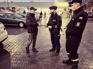 parking przed marketem, policjant wręcza odblask mężczyźnie, strażak stoi obok