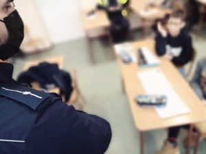 zdjęcie z wizyty policjantów w szkole - widać pagon policjanta i ławki w których siedzą dzieci