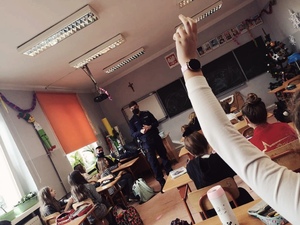 zdjęcie z wizyty policjantów w szkole - dzielnicowy prowadzi rozmowę, jedne z uczniów podniósł rękę