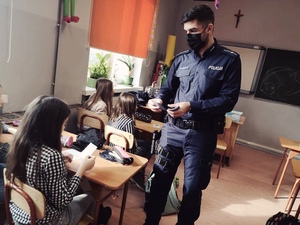 zdjęcie z wizyty policjantów w szkole - dzielnicowy rozdaje dzieciom ulotki