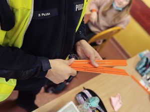 zdjęcie z wizyty policjantów w szkole - policjant z drogówki trzyma w rękach odblaskowe opaski