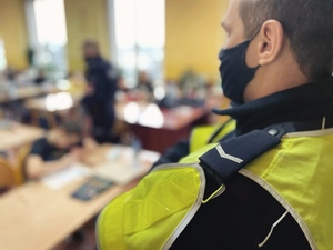 zdjęcie z wizyty policjantów w szkole - policjant z drogówki, w tle ławki szkolne w których siedzą dzieci