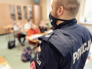 zdjęcie z wizyty policjantów w szkole - policyjny profilaktyk prowadzi pogadankę w tle dzieci w ławkach