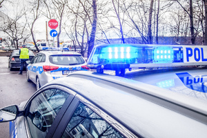 dwa radiowozy, jeden z włączonymi niebieskimi światłami, przed stoi czarny samochód i policjant obok niego