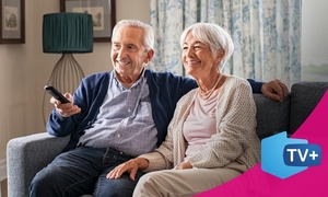 seniorzy siedzą na kanapie, mężczyzna trzyma w ręku pilota od telewizora