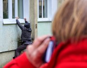 mężczyzna próbuje wejść przez okno, plecy kobiety z telefonem przy uchu