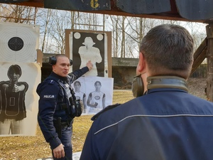 strzelnica zewnętrzna - przy tarczach instruktor, tłumaczy wyniki policjantowi na pierwszym planie