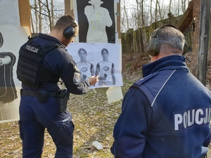 strzelnica zewnętrzna - policyjny instruktor liczy ilość trafień na tarczy policjanta stojącego przed